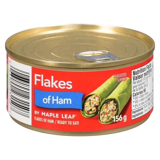 Flakes of Ham by Maple Leaf canned shredded ham in a 156 g gold metal can with pull-tab lid, featuring a red label with white and blue text, nutrition facts, and a serving suggestion of green wraps filled with ham flakes, suitable for sandwiches, salads, and soups.