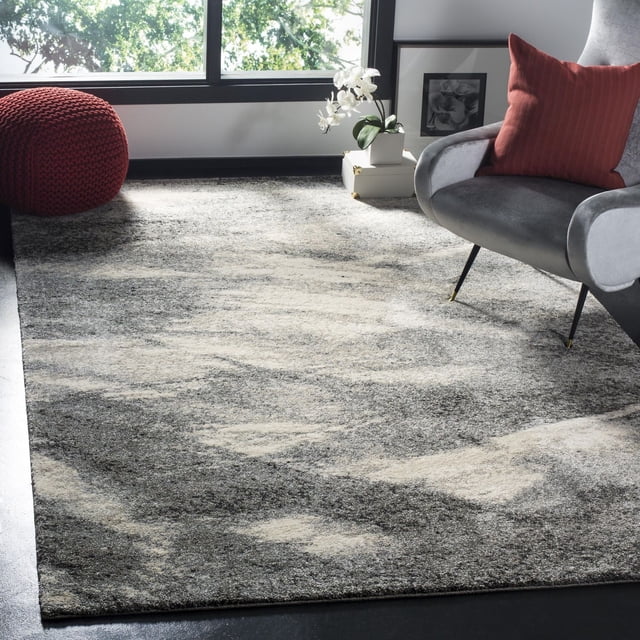 Safavieh Retro Panit Abstract Area Rug in grey and ivory with a low pile and mid-century modern abstract pattern, displayed in a bright room with a grey armchair with a red cushion, a red knitted pouf, and a white orchid on stacked boxes near a large window, ideal for complementing clean-lined furniture.