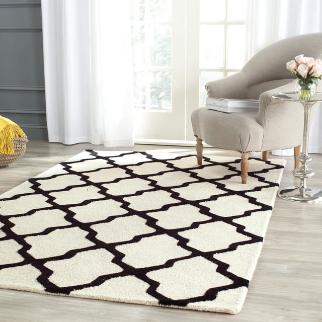 Safavieh Cambridge Tapis Géométrique Liam Mettant en Vedette une pile de Laine Crème Tuftée à la Main avec un Motif de Treillis Géométrique Noir, Exposé sur un Plancher de Bois Franc Clair sous un Fauteuil Rembourré beige et à Côté d'Une table d'Appoint Argentée avec des roses roses, Idéal pour Ajouter un style Américain Moderne aux Espaces de la Maison Ou du Bureau.