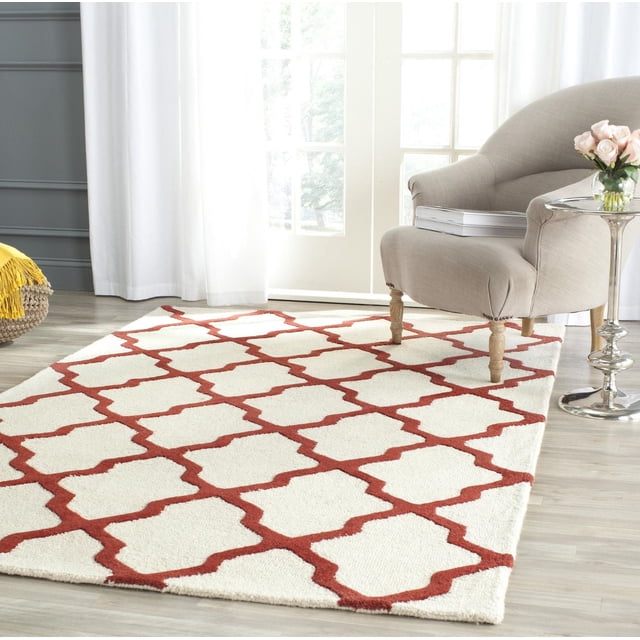 Safavieh Cambridge Tapis Géométrique Liam en Laine Tuftée à la Main avec Fond Crème et Motif de Treillis Géométrique Rouge Rouille, Montré sur un Plancher de Bois Clair dans une Pièce Éclatante avec un Fauteuil beige et une table d'Appoint Argentée avec des roses roses, Idéal pour Ajouter un style Américain Moderne à la Maison Ou au Bureau.