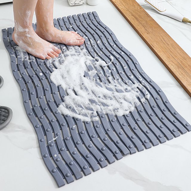 Boovnll Bathroom Rugs, Absorbent Thicken Non-Slip Backing Bathroom Mat displayed on a bathroom floor. The grey mat has a wavy texture with suction cups for enhanced grip and slip resistance. Soap suds are present, highlighting its water-absorbent and quick-drying features. Suitable for bathrooms, shower rooms, and other indoor spaces.