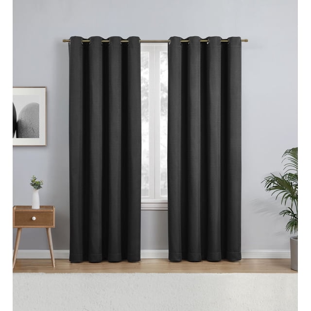 Eclipse Heath 63" Grommet Blackout Window Curtains Panel in black, hanging on a metal rod with grommet top, covering a window in a room with light grey walls and wooden floor, accompanied by a wooden side table with a small plant and a potted green plant, made of 100% polyester fabric that blocks light, reduces noise, and helps with energy savings.