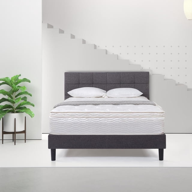 Zinus Spa Sensations 12 inch Support Spring Mattress on a dark grey upholstered bed frame with tufted headboard, featuring a quilted fiber cover and wave pattern, set against a white wall with geometric staircase design, two white pillows, and a green potted plant. It includes CertiPUR-US Certified high-density and Visco latex foams with a heavy-duty steel innerspring base, suitable for stomach sleepers seeking balanced support.