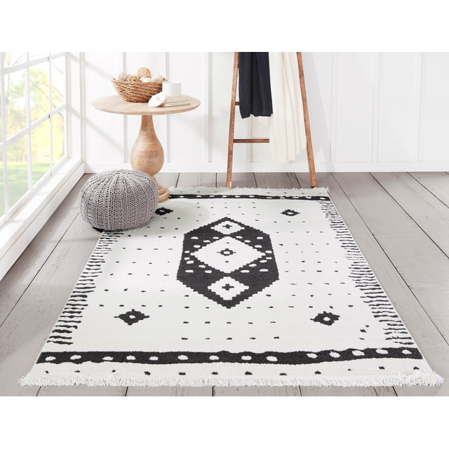 ECARPET Lyra Contemporary Area Rug in black and white featuring tribal diamond and dot patterns, placed on light wood flooring in a bright room with a wooden side table, grey knitted pouf, and wooden ladder with textiles, ideal as an accent rug for living rooms, bedrooms, or hallways.