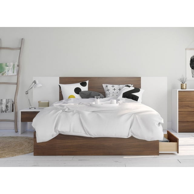 Nexera Foliage 4 Piece Bedroom Set, Walnut and White, featuring a 3-drawer storage bed with walnut finish and white melamine headboard extension panels, plus a white and walnut nightstand. The bed is styled with white bedding and black and yellow geometric pillows in a minimalist room with white walls, a wooden ladder shelf, metal desk lamp, and matching dresser. The storage drawers provide practical bedroom organization.