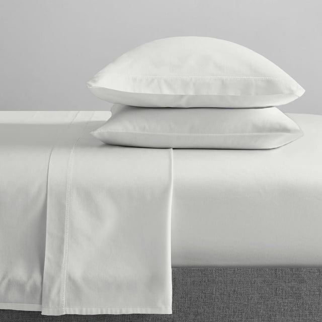 Johnson Home Huggable Jersey Knit Combed Cotton Easy Fit Sheet Set in white, showing a fitted sheet with 15-inch deep pockets, a flat sheet draped over the mattress edge, and two stacked pillowcases made of soft jersey knit fabric, suitable for a comfortable bedroom.