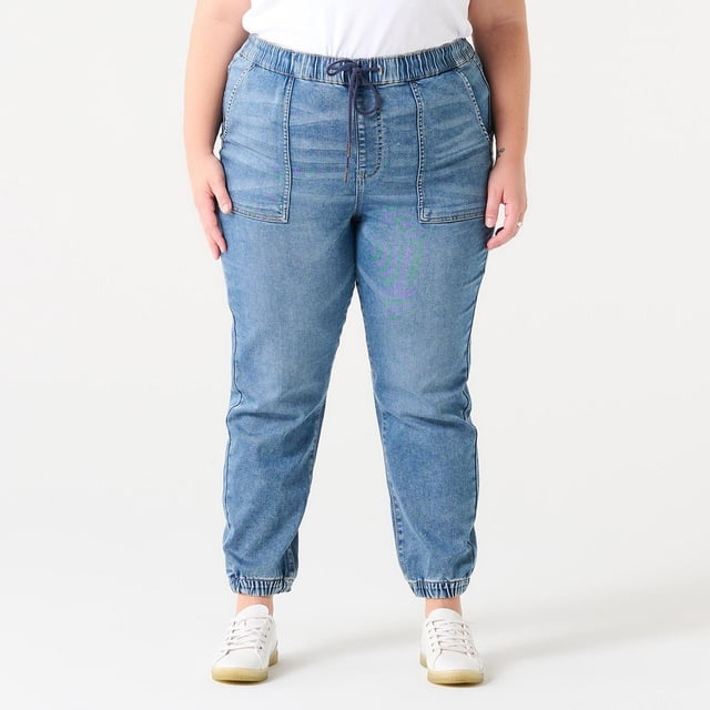 HIGH RISE DENIM JOGGER in medium blue denim featuring an elastic waistband with navy drawstring, large front patch pockets, tapered legs with elastic cuffs, worn front-facing by a person against a white background, ideal for casual wear and pairing with sneakers.