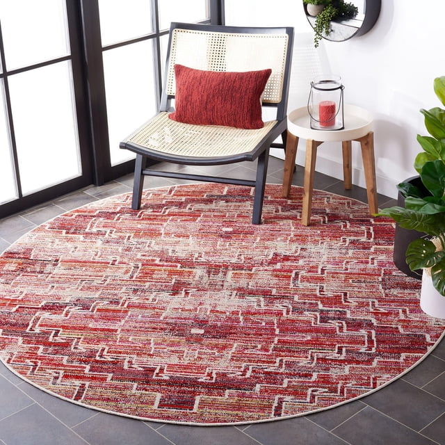 Safavieh Montage Bryon Abstract Outdoor Area Rug, round with red and beige geometric abstract pattern, power-loomed synthetic yarn for outdoor durability, placed on tiled floor under black-framed woven chair with red cushion, beside wooden side table with glass lantern and red candle, near green plants in bright room, ideal for outdoor patio or sunroom.