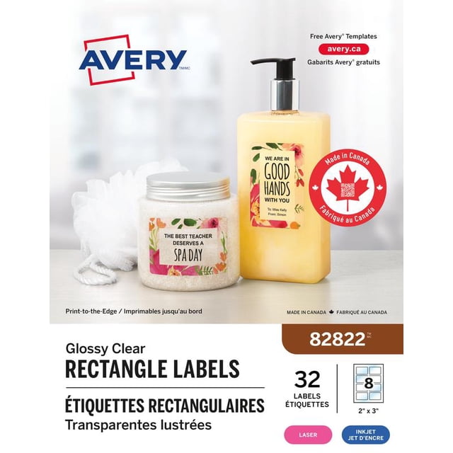 Avery 82822 Glossy Clear Rectangle Labels, 2" x 3", shown on a spa salt jar and lotion bottle with floral decorative labels reading 'The best teacher deserves a spa day' and 'We are in good hands with you', featuring permanent adhesive for smooth surfaces and compatibility with laser and inkjet printers, displayed with a white bath sponge on a light surface.