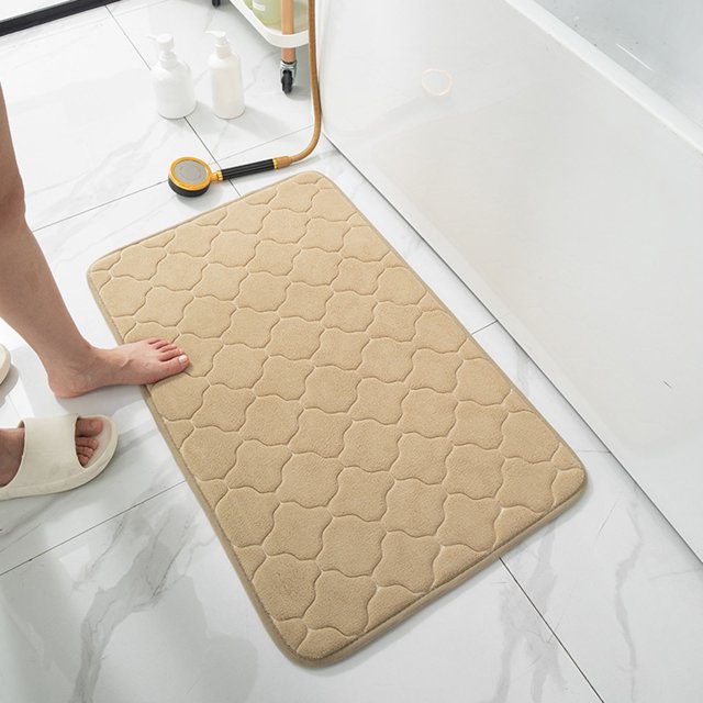 TIMIFIS Bathroom Rugs Entrance Door Mat in beige with a quilted pattern, made of soft sponge and polyester fiber. This non-slip, machine washable mat offers excellent water absorption and comfort, ideal for bathrooms, bedrooms, and other indoor spaces. Displayed on a tiled bathroom floor near a bathtub, with a foot stepping on it to demonstrate its softness and functionality.