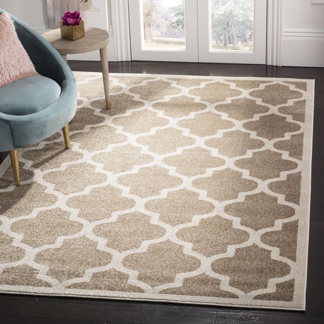 Safavieh Amherst Roderick Geometric Area Rug in beige and cream with a repeating trellis pattern, power loomed polypropylene cut pile for durable indoor-outdoor use, shown on dark hardwood floors with a blue velvet chair and a round side table with a pink flower.