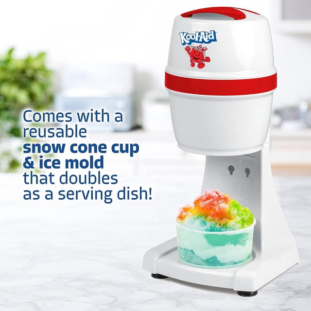 Kool-Aid Shaved Ice & Snow Cone Maker in white with red accents and Kool-Aid logo, shown on a kitchen countertop with a reusable snow cone cup filled with colorful shaved ice beneath the stainless steel blade. This small appliance is designed for making snow cones, slushies, and icy desserts, featuring an ice mold that doubles as a serving dish.