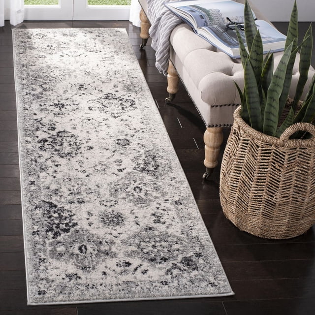 SAFAVIEH Madison Judith Geometric Floral Area Rug in a narrow runner style with a distressed grey and black floral and geometric pattern on a light background, power loomed for durability, displayed on dark hardwood flooring beside a beige tufted bench and woven basket with snake plants, ideal for transitional home decor in hallways or entryways.