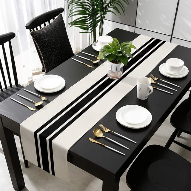 Wzzjkit Table Runner Geometric Striped Linen Table Flag with a modern black and white bitonal stripe design, ideal for dining tables, coffee tables, or home decoration. Displayed on a black dining table set with white plates, gold and silver cutlery, and a potted plant centerpiece. Made from durable linen material, it measures 182 x 33 cm (72 x 13 inches) and suits various home decor styles.
