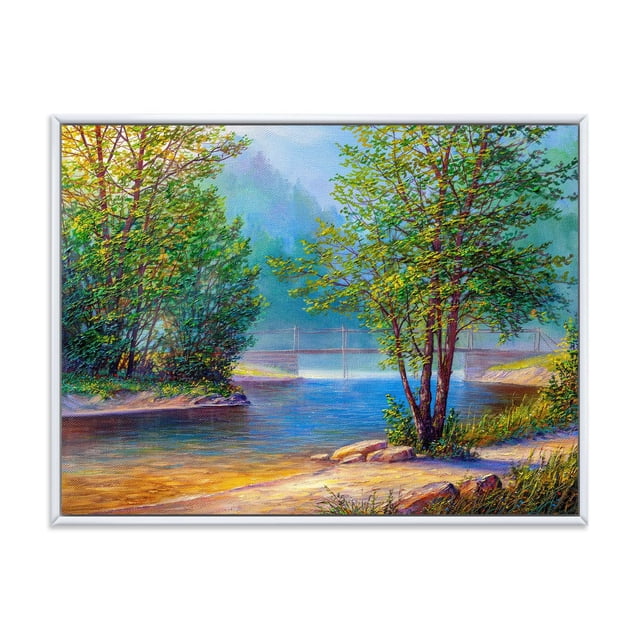 Designart Green Trees By The Riverside FLOAT FRAME WALL ART depicting a framed canvas print of a riverside landscape with green trees on sandy banks, a calm blue river flowing under a faint suspension bridge in the misty background, printed on fade-resistant cotton canvas with gallery-wrapped edges in a white floating frame, ready to hang and suitable for enhancing home décor.