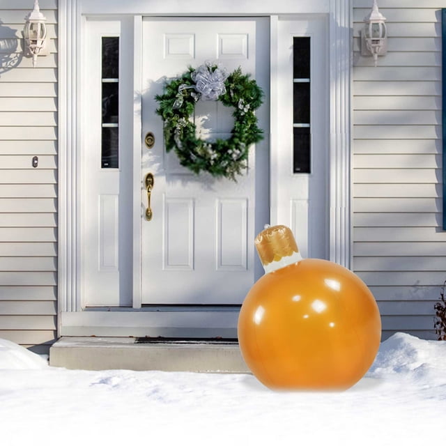Vaidha 50cm Outdoor Christmas Inflatable Decorated Ball displayed in a snowy front yard near a white door with a festive wreath. The inflatable ball has a glossy orange finish and a decorative top resembling a Christmas ornament cap, ideal for outdoor holiday decorations and Christmas inflatables.