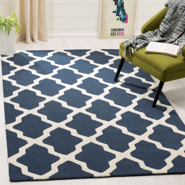 Safavieh Cambridge Liam Tapis Géométrique pour Aire en Bleu Marine et Blanc avec un Motif de Treillis Géométrique en Laine Tufté à la Main, Montré sur un Plancher de Bois Franc Clair avec une Chaise Verte Drapée d'Un Jeté Gris et un Livre Ouvert, Convient à la Déco Moderne de la Maison Ou du Bureau.