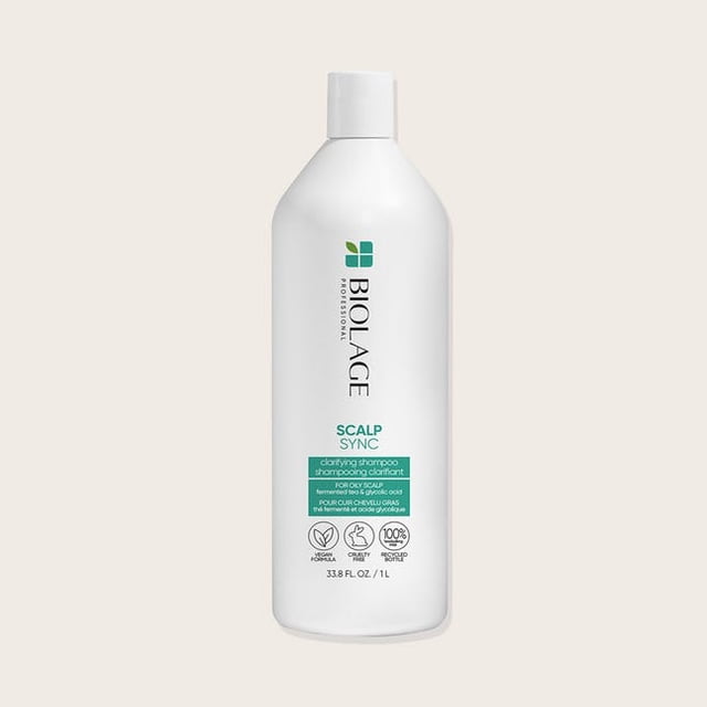 Biolage Scalp Sync Clarifying Shampoo, a gentle clarifying shampoo for oily scalps, in a 1 L bottle. The white bottle displays green and black text highlighting its benefits, such as removing residue, buildup, and excess oil. Infused with fermented tea and glycolic acid, it balances scalp moisture levels while restoring shine and volume to hair. Free from parabens, silicone, and mineral oil.