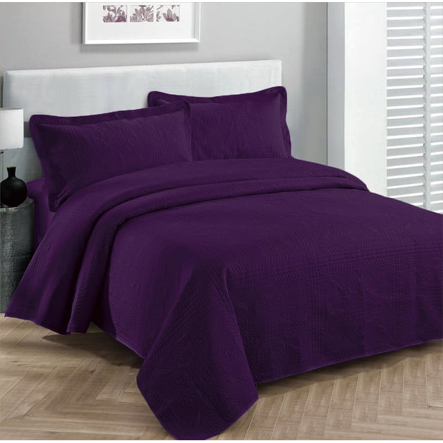 Fancy Collection Luxury Bedspread Coverlet Embossed Bed Cover in solid purple displayed on a full/queen-sized bed. The set includes an oversized bedspread measuring 100 inches by 106 inches and two matching pillow shams, each 20 inches by 26 inches. Made from 100% microfiber polyester, the bedspread features an embossed design and is machine washable. The bedding is styled in a modern bedroom with a light grey headboard and wooden flooring.