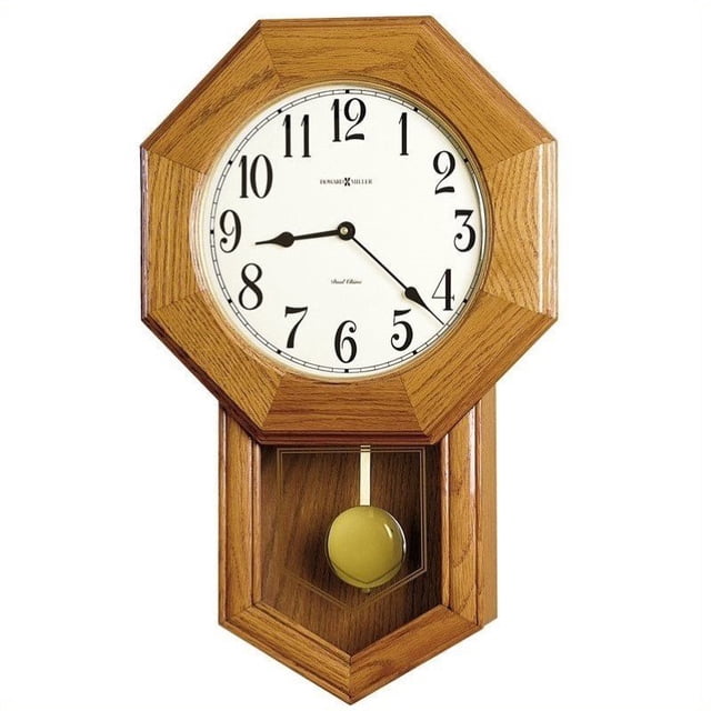 HOWARD MILLER ELLIOTT WALL CLOCK 625242 avec un design Géométrique d'Inspiration Rétro et une Finition Chêne Doré. l'Horloge Présente un Cadran Blanc Cassé avec des Chiffres Arabes Noirs et des Aiguilles Pelle, Sertie derrière un Verre Convexe en Cristal. un Pendule Ton Or Est visible à Travers le Panneau en Verre Inférieur. Comprend un Mouvement à quartz avec options Harmonique à Triple Carillon, un Contrôle du volume et Arrêt Automatique de Nuit.