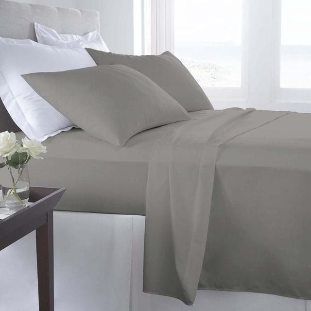 Johnson Home 500 thread count certified organic cotton sheet set in taupe on a neatly made bed with matching pillowcases, featuring smooth, breathable fabric near a window with white curtains and a dark wooden side table with white roses, suitable for enhancing bedroom comfort and style.
