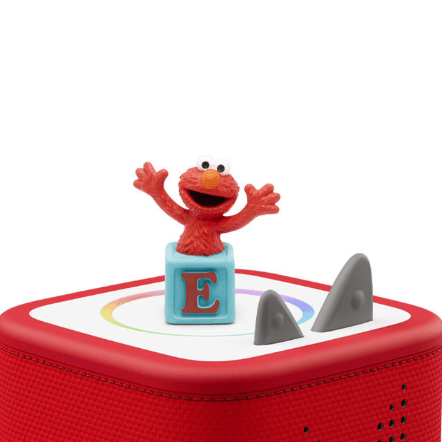 Tonies Personnage Audio - Sesame Street Elmo sur une Toniebox Rouge avec Côtés en Tissu et Deux Boutons de Commande Gris, Montrant une Figurine Elmo Rouge avec les Bras Levés sur un Bloc Bleu avec Lettre E, Conçue pour un Jeu Audio Éducatif Sans Écran pour Enfants.