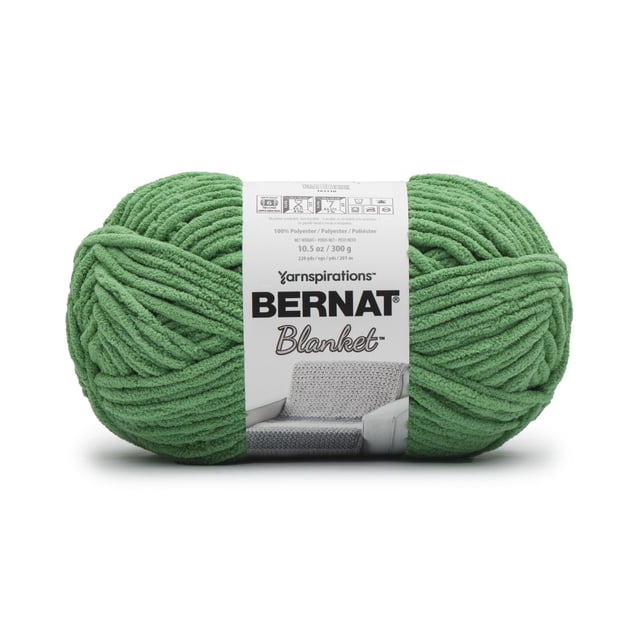 Bernat® Blanket™ #6 Super Bulky Polyester Yarn 10.5oz/300g in green, a chenille-style soft yarn ball with thick strands, wrapped with a label showing care instructions and a grey knitted blanket on a chair, suitable for fast knitting and crochet home décor projects like blankets and baskets.