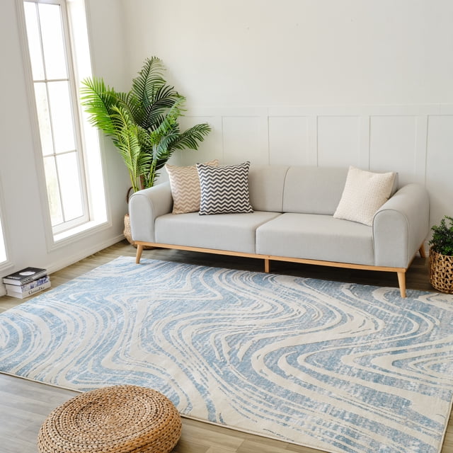 Rug Branch Nomad Abstract Indoor Area Rug, Blue Beige, Coastal style, 8'x11' (7'10" x 10'10"), featuring swirling blue and beige abstract patterns on light wood flooring in a bright living room with a light gray sofa with wooden legs and three decorative pillows, a tall green plant by a window, and a woven basket planter, suitable for living room, bedroom, dining room, or kitchen.
