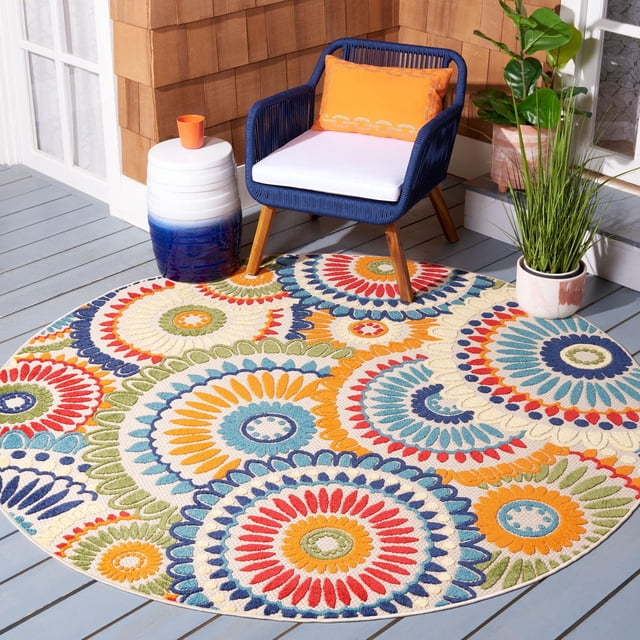SAFAVIEH Cabana Marina Suzani Tapis d'Extérieur de Forme Ronde avec des Motifs Floraux et Géométriques Suzani Colorés en Rouge, Bleu, orange, Vert et Crème sur une Terrasse en Bois Gris Pâle. le Tapis d'Extérieur Est Assorti à un Fauteuil Tressé Bleu Marine avec Pattes en Bois, un Coussin Blanc et un Oreiller orange. À Proximité, une table d'Appoint en Céramique Blanche et Bleue avec une Tasse orange et Deux Plantes Vertes en Pot, Améliorant l'Ambiance du patio. Ce Tapis d'Extérieur durable Est Idéal pour les Espaces Extérieurs Occupés comme les Terrasses et les porches