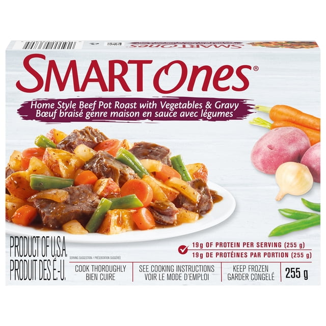 Smart Ones Homestyle Beef Pot Roast Frozen Meal with beef pot roast, carrots, green beans, and potatoes in gravy on a white plate, accompanied by fresh carrots, red potatoes, garlic, and green beans on a light wood background, 255g package with 19g protein per serving, suitable for a quick microwave meal.
