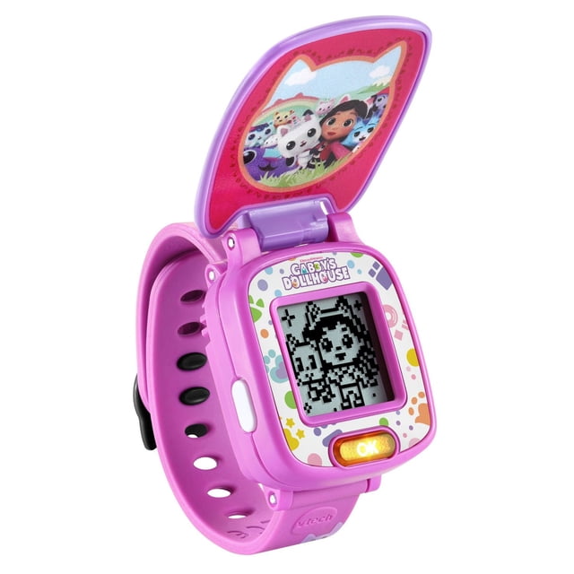 VTech Gabby’s Dollhouse Time to Get Tiny Watch with Games - English Version, a bright pink educational electronic wristwatch for kids featuring a flip-up cover with Gabby and Pandy Paws. The digital screen displays a pixelated character from the show, surrounded by colorful polka dots on the bezel and an orange OK button below. Includes 10 clock faces, four games, alarm, timer, and stopwatch, suitable for children aged 3 and up.