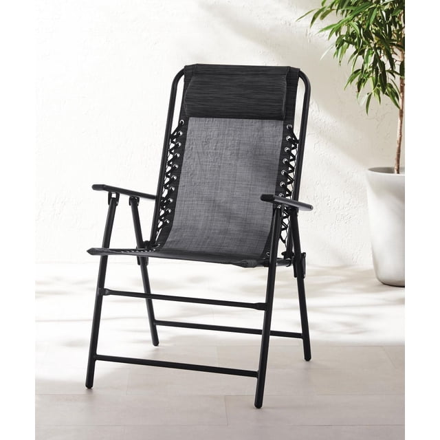Mainstays Folding Bungee Chair with black powder-coated steel frame and quick-dry, UV-resistant fabric sling, padded headrest, and bungee cord sides, designed to fold for easy storage, shown indoors near a potted plant.