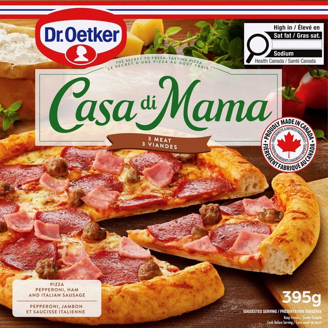 Dr. Oetker Casa di Mama 3 Meat Pizza with rising crust topped with pepperoni, smoked ham, and Italian sausage on spiced tomato sauce and melted cheese, sliced on a wooden board with fresh herbs and cheese blocks in the background, made in Canada from domestic and imported ingredients.