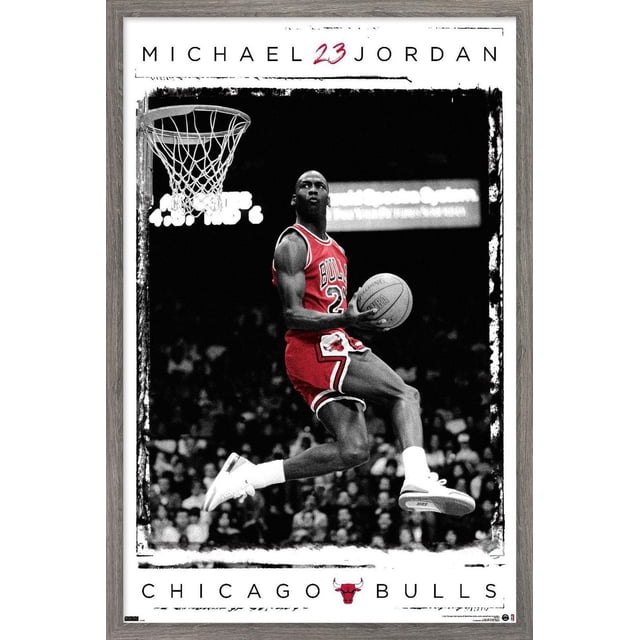 Michael Jordan - Dunk Wall Poster, 14.725" x 22.375" Framed showing Michael Jordan in a red Chicago Bulls jersey number 23 mid-air holding a Spalding basketball near the hoop during a dunk, with a black and white crowd background and light wood frame.
