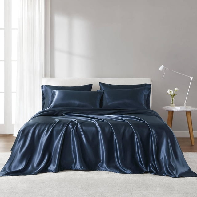 Madison Park Essentials Ensemble de Draps en Satin Bleu Marine sur un Lit avec une Tête de Lit Rembourrée Blanche, Comprenant des Draps Plats et Ajustés en Satin Infroissables et Quatre Taies d'Oreiller à texture Lisse et Soyeuse Qui Réduisent les Frisottis des Cheveux et la friction de la Peau, Exposé dans une Chambre Moderne avec des Murs Gris Pâle, une Lampe sur Pied Blanche et une table d'Appoint en Bois avec des Fleurs Blanches.