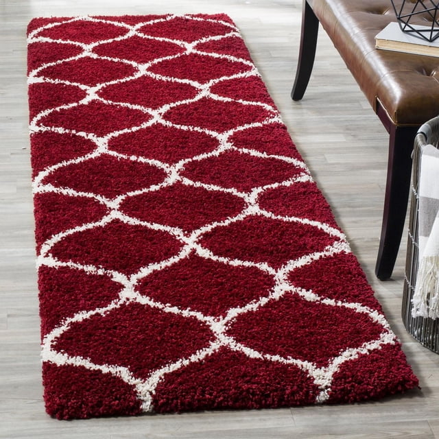 Safavieh Hudson Arline Geometric Shag Area Rug with deep red plush shag pile and white onion-shaped tile pattern, shown on light hardwood floor beside brown leather bench and basket with throw, ideal for adding durable texture to modern living spaces.