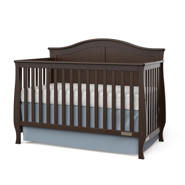 Berceau Convertible pour Enfant en Fini Bois Foncé avec Dessus Arqué Doux, Pattes Évasées et Lattes Verticales, Doté d'Un Matelas Blanc à Motif Floral, Construit avec un support de Matelas en Métal Ajustable et une Finition Non Toxique, Conçu pour Se Convertir du Berceau au Lit pour Tout-Petit, au Lit de Jour et au Lit Double.