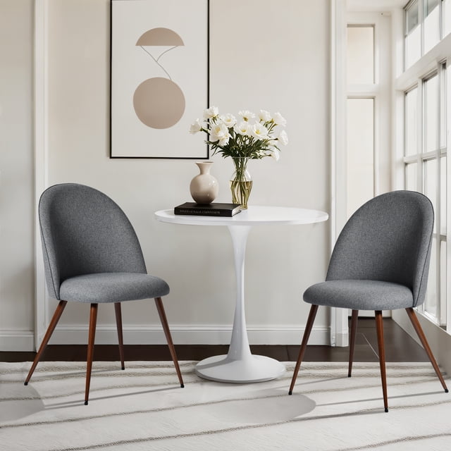 Homy Casa 2-Pack Armless Upholstered Accent Chairs with Round Back in grey fabric, featuring padded seats and gently rounded high backs, supported by walnut-style metal legs, arranged around a white round pedestal table with a beige vase, a book, and a glass vase of white flowers in a sunlit minimalist living room. Their compact design is suitable for small spaces and corners.