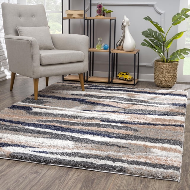 Rug Branch Retro Collection Modern Abstract Area Rug in grey with plush shag texture and horizontal stripes in white, beige, navy, and charcoal on wood flooring beneath a light grey armchair with wooden legs, beside a black metal and wood shelf with decor and a woven basket planter with green leaves, suitable for modern family rooms and high-traffic areas.