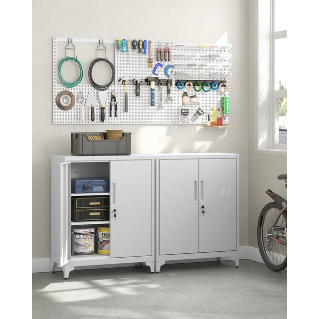 SONGMICS Garage Cabinet, a matte gray metal storage cabinet with doors and adjustable shelves, shown in a garage setting. The cabinet is lockable with a sturdy steel lock and includes two keys for secure storage. One cabinet door is open, revealing organized items such as tools, paint cans, and storage boxes. The cabinet is constructed from rust-resistant, powder-coated steel, ensuring durability and water resistance. It measures 15.7 inches deep, 31.5 inches wide, and 35.4 inches high, making it suitable for storing tools, files, or household items. The cabinet is placed against a wall with a pegboard above it, displaying various tools, and a bicycle is partially visible to the side.