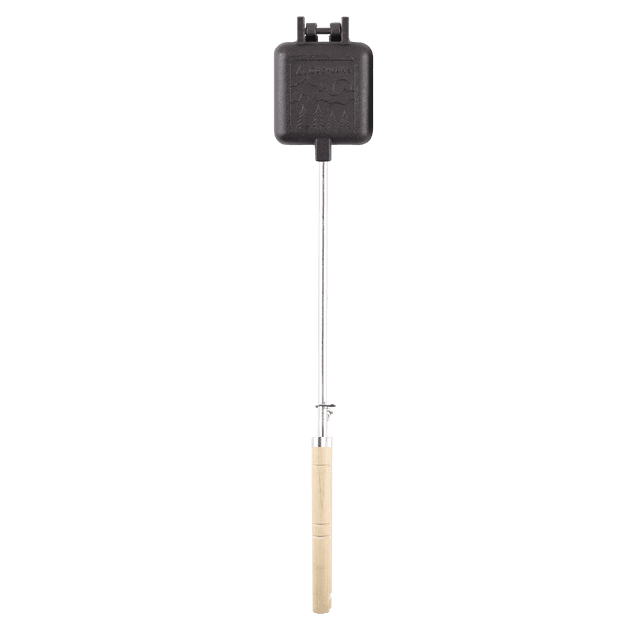 Coghlan's Pre-Seasoned Cast Pie Iron Camp Cooker with Removable Heat-Resistant Handles, featuring a square black pre-seasoned cast iron cooking surface with embossed mountain and tree design, attached to a long metal handle with a light wooden grip and S-clip lock near the reinforced hinge, designed for even heat distribution and easy outdoor campfire cooking.