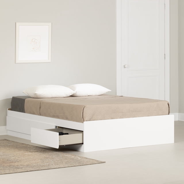 South Shore Fusion Full Mates Bed with 3 Drawers in pure white, shown in a neutral bedroom with beige walls and a white door. The platform bed features a low-profile frame with three large reversible storage drawers on metal slides, one drawer open revealing storage space. The bed is dressed with a taupe coverlet and two white pillows, placed on a light floor with a beige rug nearby. Ideal for maximizing bedroom storage without needing a box spring.