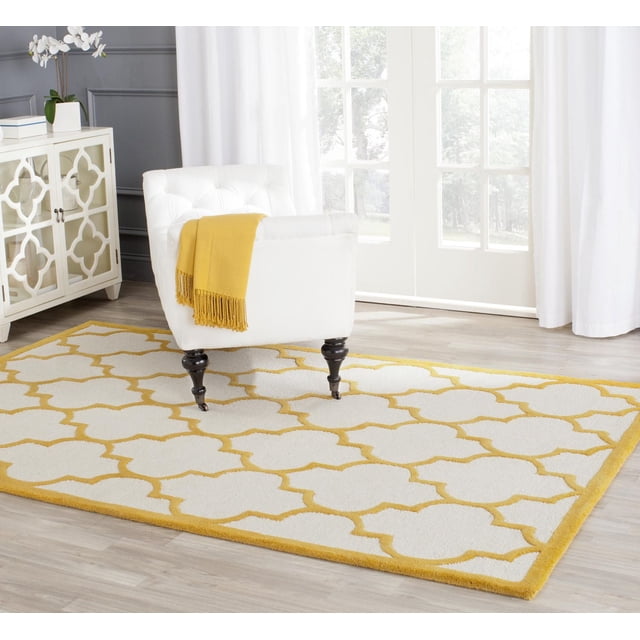 Safavieh Cambridge Kevin Tapis Géométrique Mettant en Vedette un Motif Géométrique Blanc et Jaune avec une Bordure Jaune, Exposé sur un Plancher de Bois Clair sous un Fauteuil Capitonné Blanc avec un Jeté Jaune, dans une Pièce Lumineuse avec des Rideaux Blancs et une Armoire Miroir, Idéal pour Ajouter un style et une texture Américains Modernes à la Déco de la Maison.
