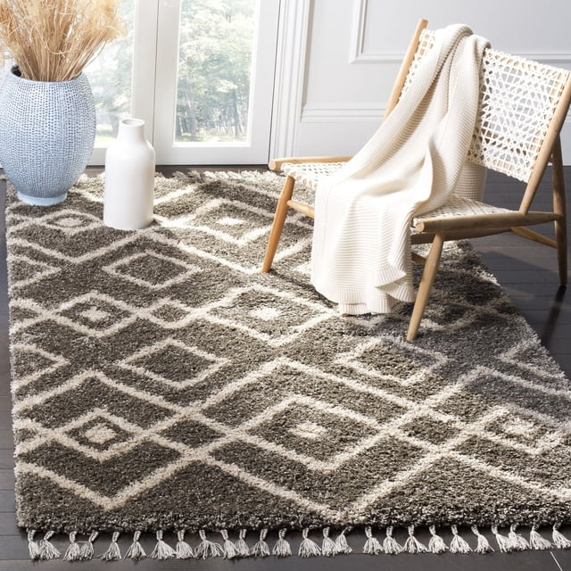 Safavieh Moroccan Fringe Shag Janella Tapis Géométrique Présentant une texture Shag Synthétique Pelucheuse avec un Motif tribal en Losanges et des Bords à Franges, Conçu sur un Plancher de Bois Franc Foncé sous une Chaise en Bois Tressée Drapée avec un Jeté en Tricot Crème, Près de vases Décoratifs dans une Pièce Lumineuse.
