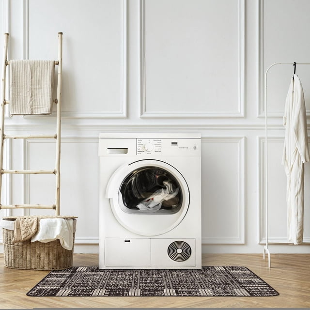 ECARPET Kitchen, Hallway, Laundry Room, Entrance, Kids Room, Bathroom Mat & Utility Rug with non slip rubber backing placed in front of a white front-loading washing machine on light wood flooring. The rug has a geometric black and white pattern and is set in a minimalist laundry room with a natural wood ladder holding a beige towel, a wicker basket with linens, and a white robe hanging on a metal rack. This durable polypropylene rug is suitable for high traffic areas and often used as a decorative floor covering in laundry spaces.