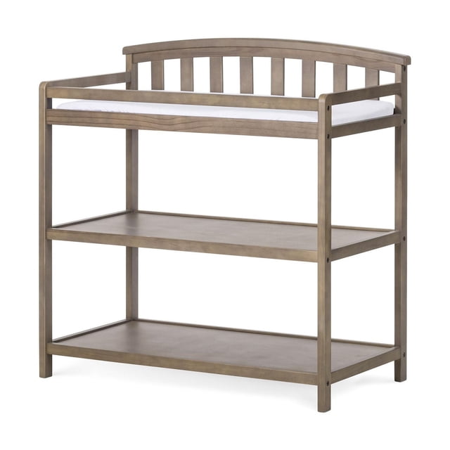 Forever Eclectic Curve Top Changing Table in natural wood finish with curved top rail and vertical slats, two open shelves for nursery storage, and a white changing pad, designed as traditional baby furniture for organized diaper changing.