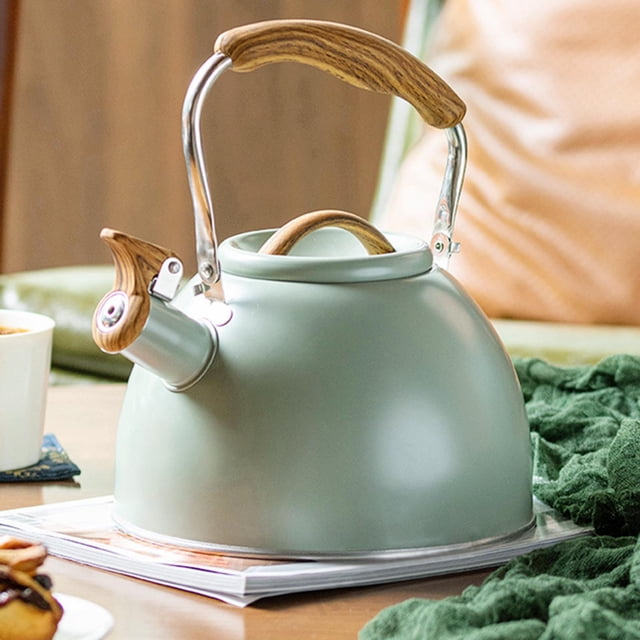 Kitchen Whistling Kettle Teapot Kettle 3L Large Capacity with Wooden Handle in light green. Made of durable, food-grade stainless steel with a rust-resistant finish. Features a wooden handle for comfortable grip and a built-in whistle for audible alerts when water boils. Suitable for all stove types and designed for uniform heating. The kettle has a 3L capacity, ideal for family use. Shown on a table with a cozy setting, including a green cloth and a cup of tea.