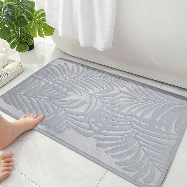 EGNMCR Bathroom Water Absorbent Door Mat in a solid gray color with a textured leaf pattern, measuring 40x60cm (15.74x23.62in). Made of polyester with a rubber backing, this quick-dry, non-slip rug is designed for use in bathrooms, shower rooms, or entrances. The mat is shown placed on a tiled bathroom floor near a bathtub, with a foot stepping onto it, highlighting its soft and absorbent surface.