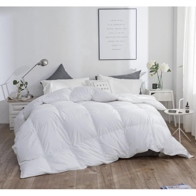 Royal Elite All Seasons European White Down Duvet with white baffle box stitching on a bed, featuring a 100% down-proof cotton shell and RDS certified European white duck down fill. Displayed with gray and white pillows in a minimalist bedroom with wooden flooring, bedside tables, plants, and a framed motivational quote. Ideal for year-round warmth and breathable comfort.