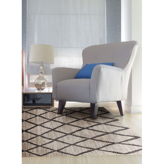 Light tan and brown woven area rug featuring a black diamond pattern placed beneath a gray upholstered armchair with wooden legs, complemented by blue cushion, lamp on side table, and light wood flooring.